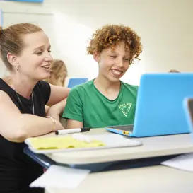 Leerkracht en leerling primair onderwijs achter laptop Leerkracht en leerling primair onderwijs achter laptop