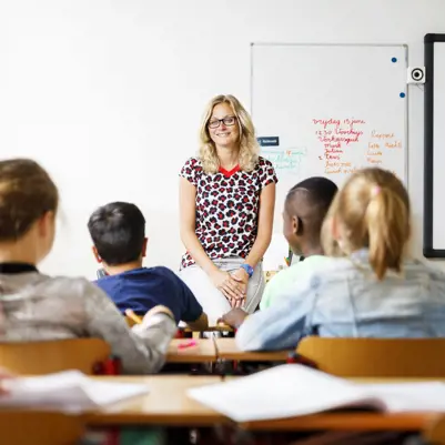 Juf zit op een tafeltje voorin de klas tevreden kijkend naar haar basisschoolleerlingen Juf zit op een tafeltje voorin de klas tevreden kijkend naar haar basisschoolleerlingen