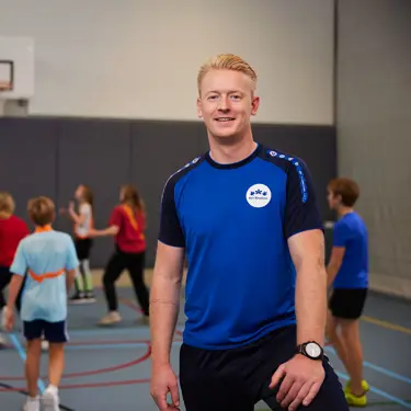 Richard Brandsma met op de achtergrond leerlingen die basketballen Richard Brandsma met op de achtergrond leerlingen die basketballen